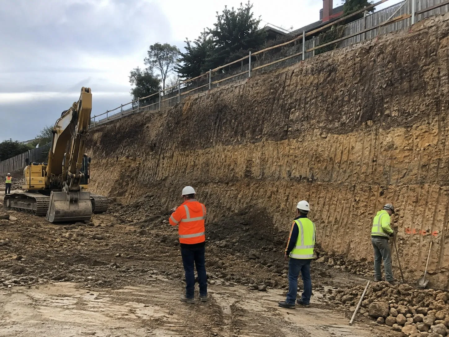 Excavation crew and digger at a battered cut face prepared for a retaining wall in Auckland